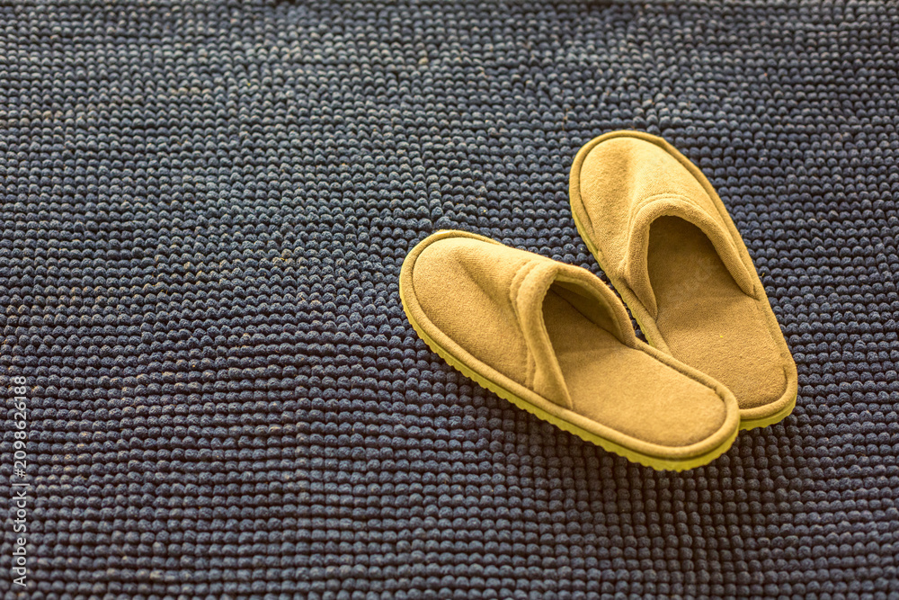 Fototapeta premium Pair of Yellow Mustard Soft Suede Slippers on Dark Navy Blue Bobble Bath Mat