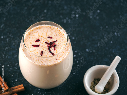 Traditional spiced milk beverage Sardai with saffron threads on top. Served in a glass on a dark background with mortar and cinnamon sticks. Copy space, perfect for Holi celebration marketing