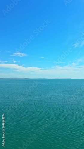 The scene shows a vast body of water under a bright blue sky. The sunlight reflects off the surface, creating soft ripples. Distant land is visible along the horizon near the water.