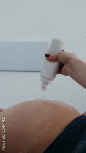 Handheld ultrasound probe applying gel on pregnant belly during prenatal checkup