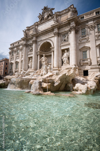 The majestic Trevi Fountain with crystal clear turquoise water in the foreground under sunny sky in Rome, Italy