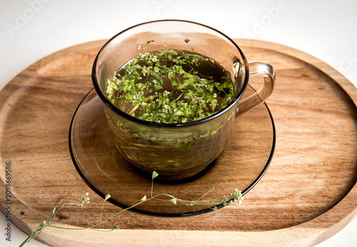 Herbal medicinal flower plant Capsella bursa-pastoris, commonly known as shepherd's purse or lady's purse small herbal medicinal flower. Herbal tea inside glass mug on wood tray.