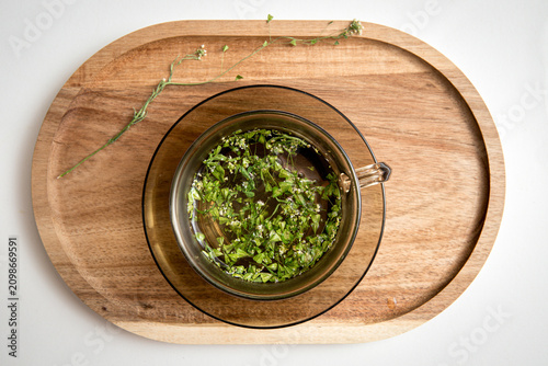 Herbal medicinal flower plant Capsella bursa-pastoris, commonly known as shepherd's purse or lady's purse small herbal medicinal flower. Herbal tea inside glass mug on wood tray.