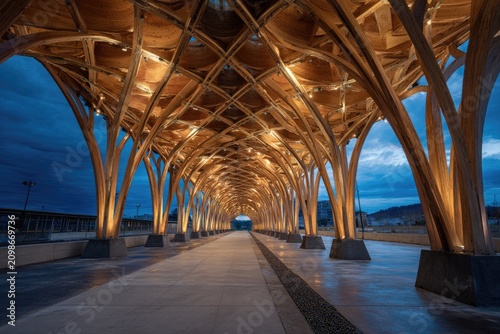 Long perspective view of a wooden architectural structure, illuminated at dusk with a walkway