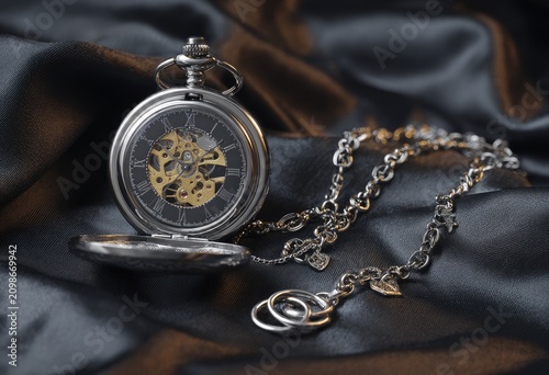 A shiny, intricate pocket watch rests on a dark, rippled fabric with an elegant chain