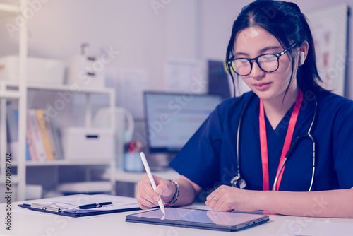 Quadro su tela Young female healthcare professional wearing medical scrubs and a stethoscope uses a digital tablet to update electronic health records in a modern clinic