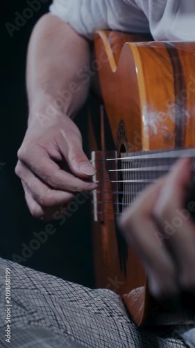 Male musician fingerpicks acoustic guitar while seated in relaxed studio setting