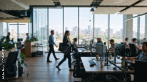Blurred background of a bright, modern open-plan office with employees working and city views.