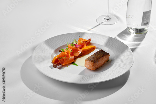 Seared salmon with carrot ribbons on white plate. Sunny minimalist fine dining table setting.