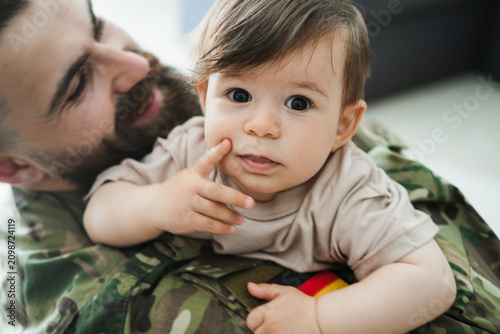 Male german soldier in military uniform hugs his little son at home - Emotional military happy homecoming concept - Soft focus on kid face