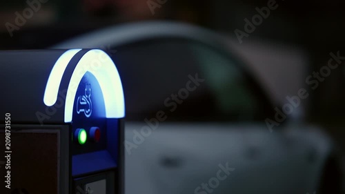 Electric vehicle charging station with green indicator light, showing a car parked in the background for eco-friendly transport