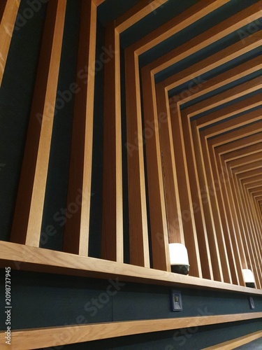 A modern interior showcasing a wooden slat ceiling with repeating geometric pattern, warm lamps and strong perspective lines. The design emphasizes texture, rhythm and contemporary architectural style