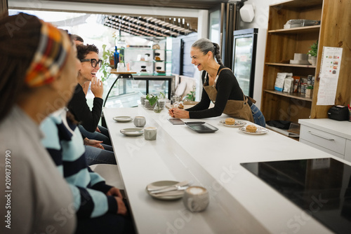 Multiracial people eating inside breakfast bar during morning time - Healthy food and morning lifestyle concept - Main focus on female waitress