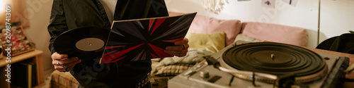 Fotografie Header of unrecognizable musician holding vinyl record and album sleeve at home, curating music collection and analog listening concept