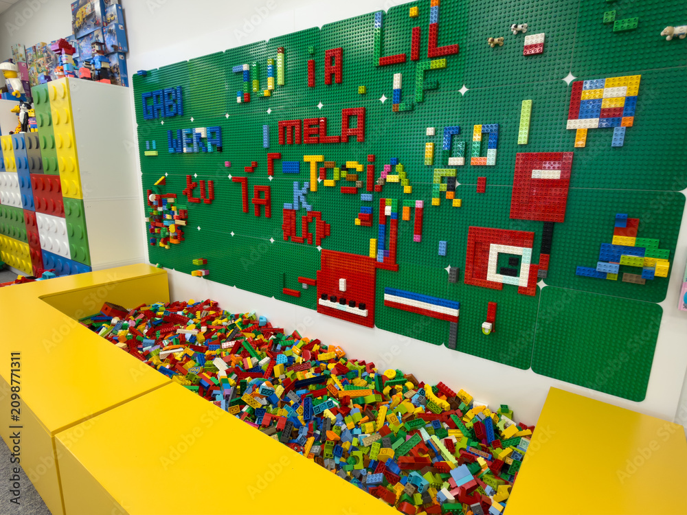 Obraz premium Colorful lego bricks in a yellow bin with a green brick wall in a children's play area, showing a creative building and toy activity space