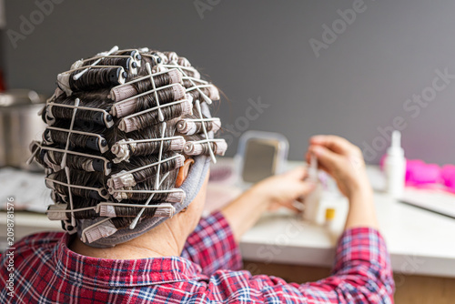 Woman prepares a permanent wave at home with perm rollers while reading the instruction manual. DIY hair care represents independence, self care, home beauty routines, and confidence in personal groom