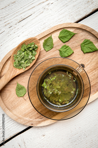 Dried Birch tree leaf powder tea drink in glass cup, Betula powder on a wood spoon on white wood board background.