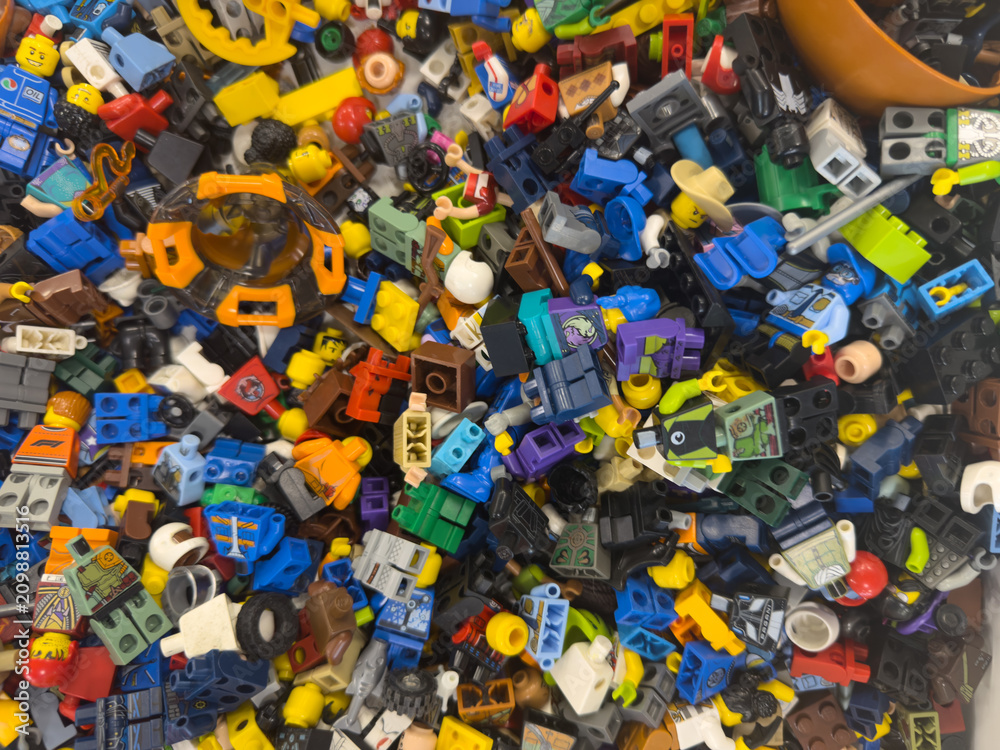 Fototapeta premium Colorful pile of assorted lego minifigure parts and accessories scattered in a mixed toy collection, viewed from above