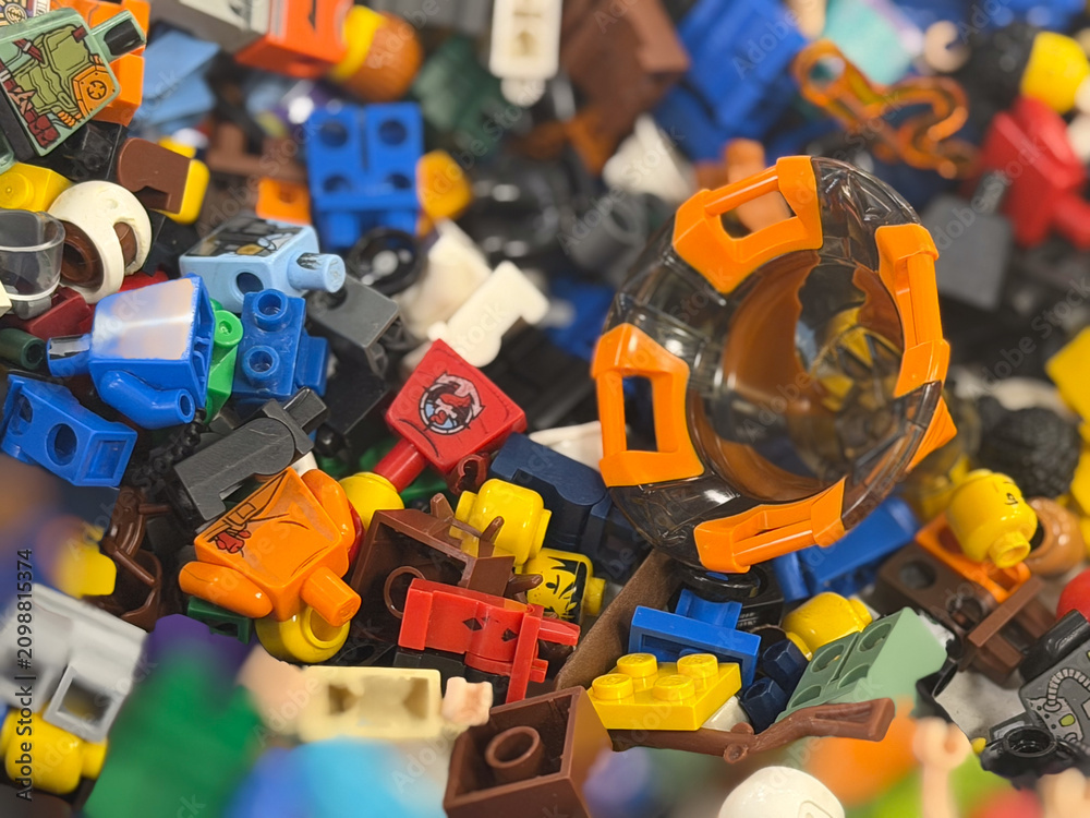 Fototapeta premium Close-up of a colorful pile of toy building bricks and minifigure parts, with an orange helmet piece among scattered plastic pieces