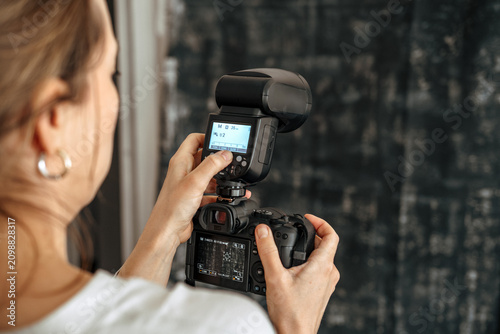 Female Photographer Adjusting External Flash on DSLR Camera During Indoor Studio Photoshoot