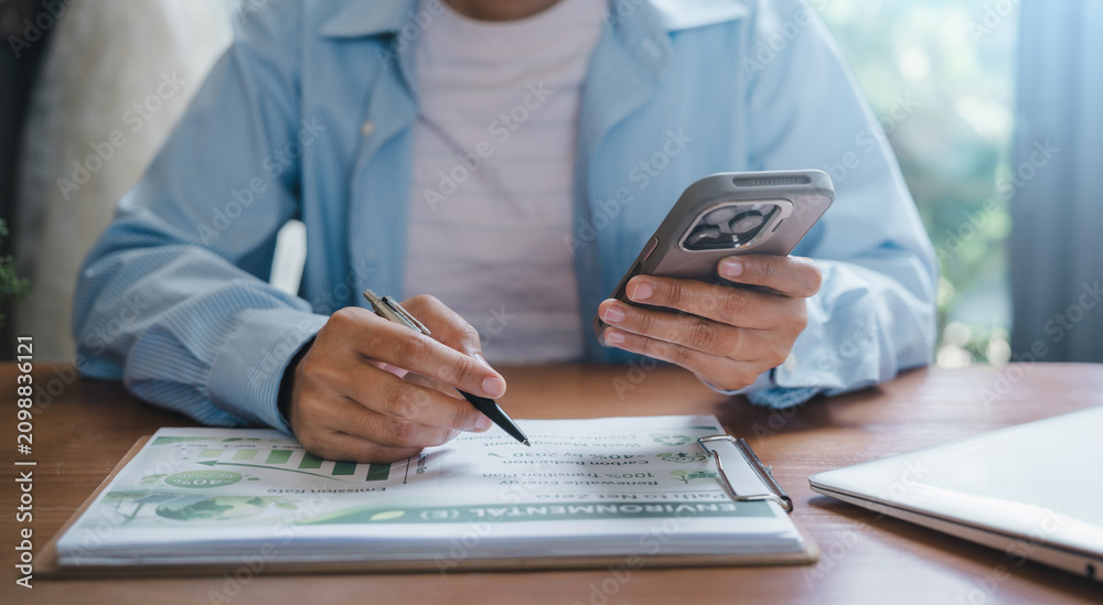 Fototapeta premium ESG report environmental social corporate governance concept business person using smartphone and pen analyzing sustainable development carbon reduction net zero data document at office desk