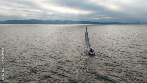 Sailing Yacht on Calm Open Sea Under Dramatic Cloudy Sky with Sun Rays