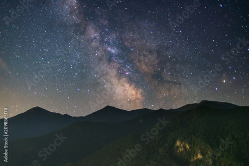 Milky Way rising above rugged Italian Alps with countless stars illuminating mountain silhouettes during clear summer night, showcasing pristine dark sky landscape and astrophotography