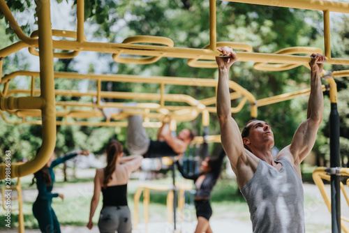 Canvas Print A young man performs pull-ups on yellow monkey bars in a sunny outdoor park gym