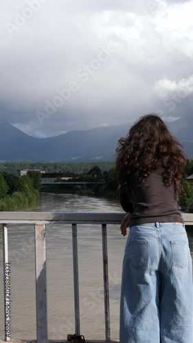 Woman with curly hair looking out over river toward misty mountains