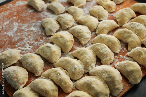 Cuadro en lienzo Hand-made raw dumplings dusted with white flour arranged on a rustic wooden board, capturing the authentic process of traditional home cooking