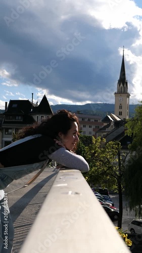Young woman leaning on a bridge railing above an alpine town, smiling