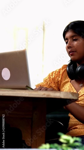 Indian Asian teenage girl studying online at home using a laptop computer while sitting by a bright, airy window in a cozy lavish home, focused on education, exam preparation, learning with dedication