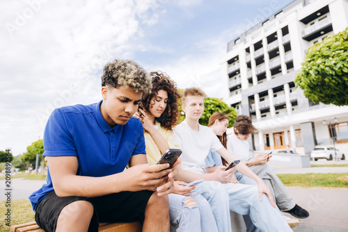 Obraz na plátně Teenagers sitting outdoors absorbed in smartphones and social media