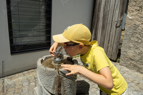 Thirsty child refreshing himself with cold water from city public drinking fountain