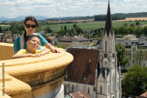 Happy mother and her young son enjoying panoramic city view from a historic balcony in summer