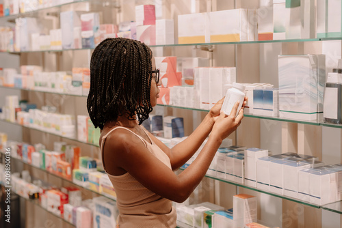 Woman choosing skincare product from shelf in beauty store reading label before purchase