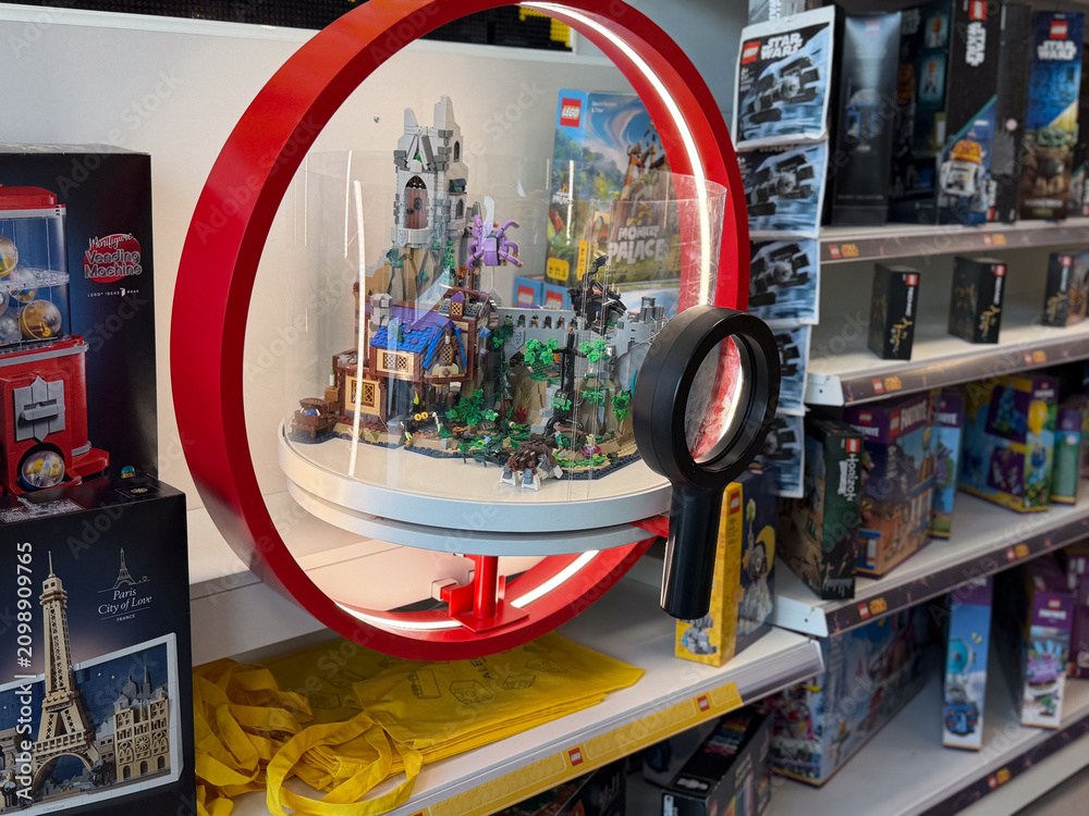 Fototapeta premium Toy store shelf with a displayed building block model under a red circular frame, surrounded by boxed construction sets and a magnifier in the foreground.