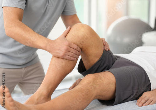 Physiotherapist examining knee of man during rehabilitation session. Professional manual therapy for joint recovery. Medical treatment and muscle stretching in clinic for healthcare support.