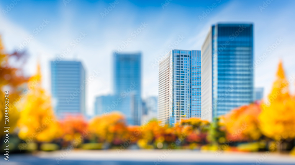 Fototapeta premium ビルと紅葉の木々に囲まれた青空広がる秋のぼかし都市風景