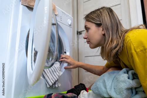 housewife loading laundry into a white washing machine in a modern bathroom. Household chores, domestic routine, and home lifestyle.