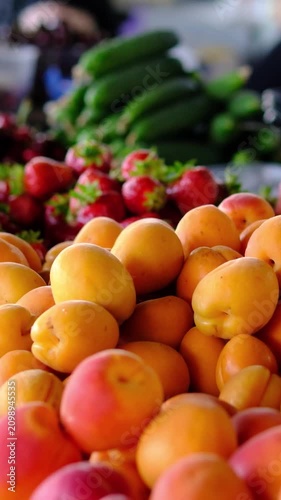 Fresh apricots strawberries and sweet cherries at farmers market as vendor arranges fruit containers on colorful summer produce display