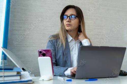 Foto Woman touching her neck, looking away from her laptop with an uncomfortable expression