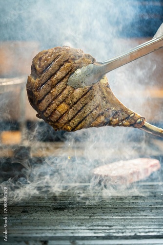 Juicy tomahawk beef steak being grilled over open fire with rising smoke