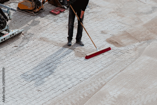 Worker sweeping sand into paver joints during patio installation