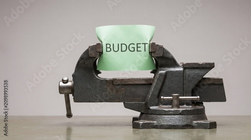 Budget squeezed in a vice, representing financial pressure and economic hardship.