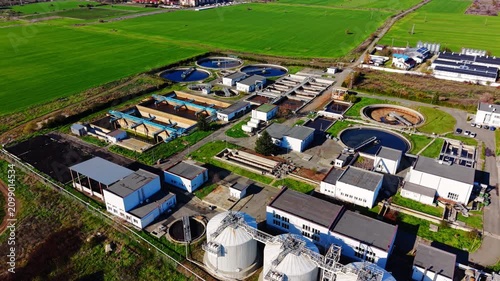 Aerial view of a treatment plant with storage silos, Bulgaria. Drone shot of cylindrical tanks, solar panels, green fields and access roads at a rural site.