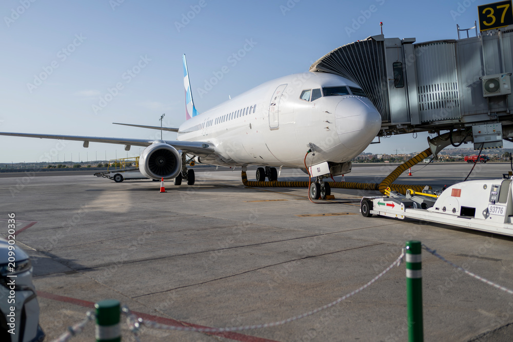 Fototapeta premium Commercial passenger aircraft connected to jet bridge at airport gate during boarding preparation with ground support equipment ready for international travel and modern aviation operations
