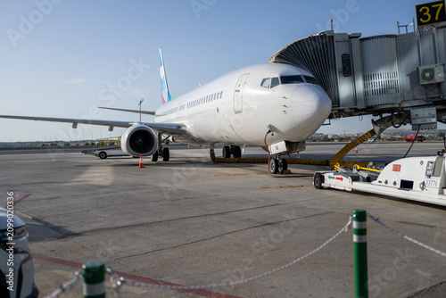 Commercial passenger aircraft connected to jet bridge at airport gate during boarding preparation with ground support equipment ready for international travel and modern aviation operations