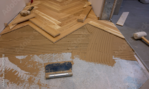 Installing oak herringbone parquet flooring with adhesive during residential interior renovation and hardwood floor construction