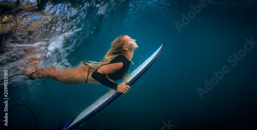 Dynamic underwater view of blonde woman paddling surfboard to catch wave